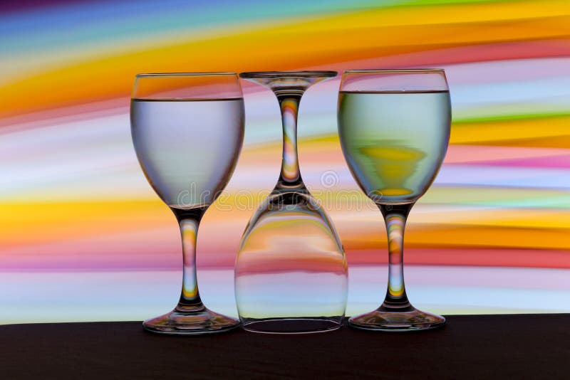 Drie wijnglazen op een rij met een regenboog van kleur achter hen royalty-vrije stock foto Drie wijnglazen op een rij met een regenboog van kleur achter hen royalty-vrije stock foto
