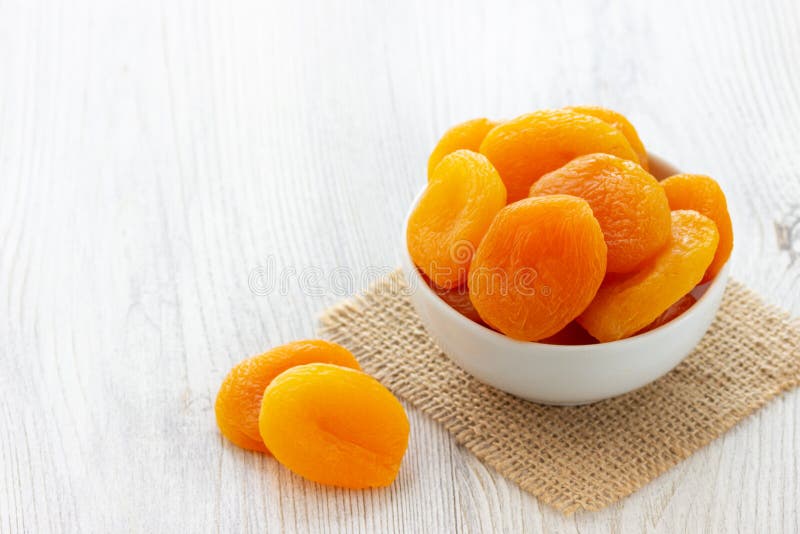 Dried apricots in a bowl on light wooden background