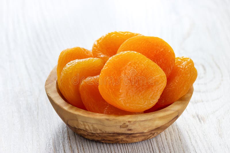 Dried apricots in a bowl on light wooden background