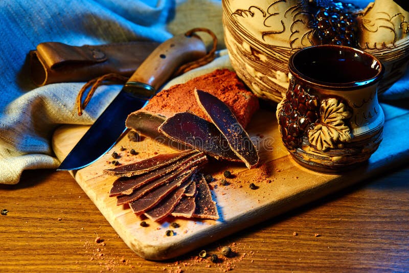 Dried meat, basturma lies on a wooden Board with capers and spices. Nearby is a clay jug and a mug stock images Dried meat, basturma lies on a wooden Board with capers and spices. Nearby is a clay jug and a mug stock images