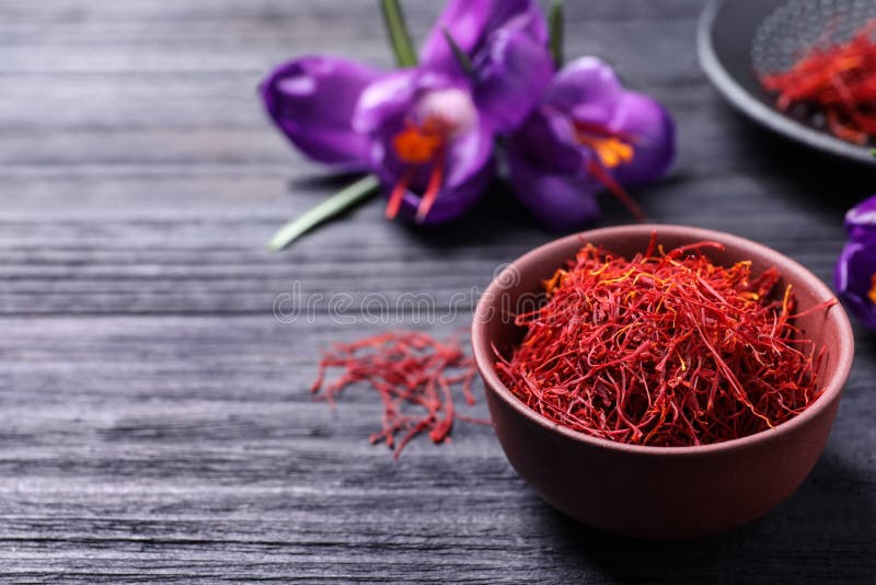 Dried saffron in bowl and crocus flowers on black wooden table, space for text royalty free stock images