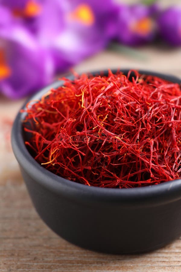 Dried saffron in bowl and crocus flowers on wooden table, closeup stock photos
