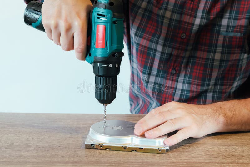 Drilling a Hard Disk Drive to Destroy Evidence Data close up.Cropped image of hand drilling on hard drive at table