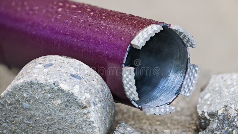 Closeup of wet purple core drill bit and cylindrical bored piece of gray concrete tile