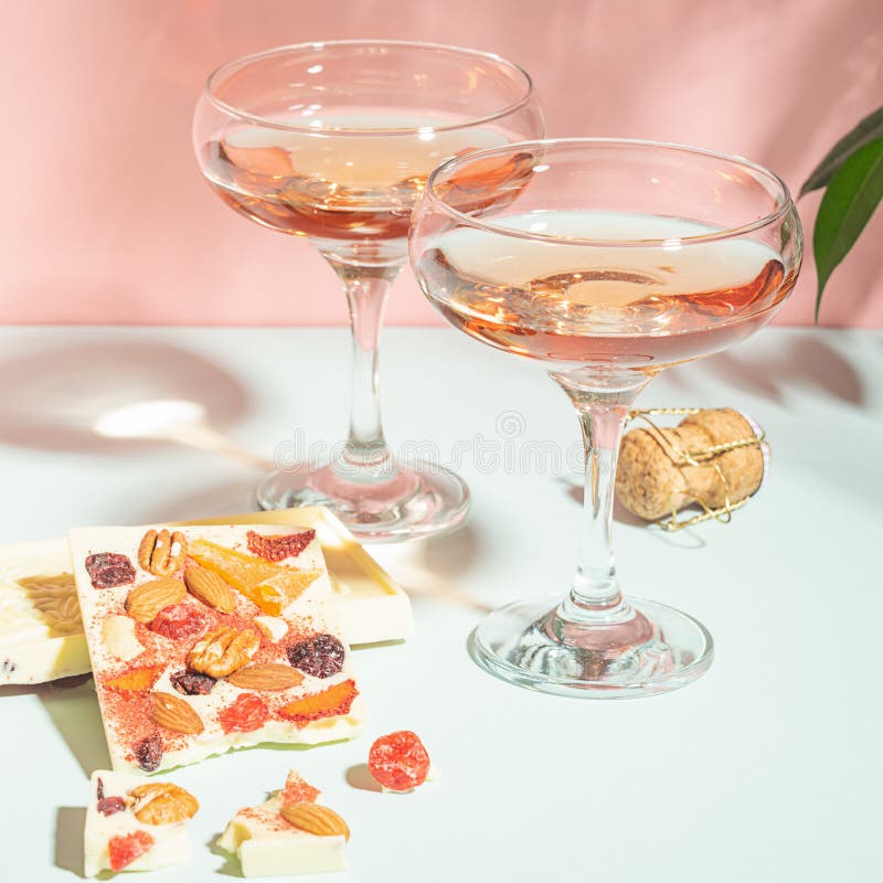 Drink champagne or wine in two elegant glasses and a bar of white chocolate. Gentle pink background bright sunlight.