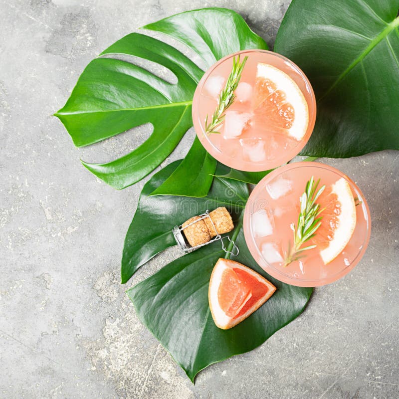 Drink grapefruit rosemary and ice in two elegant glass goblets on gray concrete background. Square frame View from above