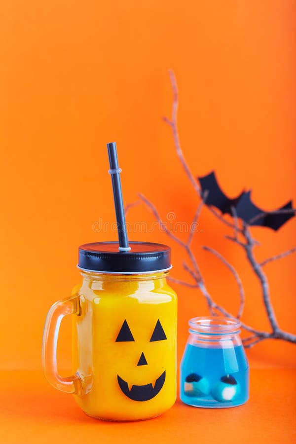 Drinkt de de gezonde pompoen of wortel van Halloween in de glaskruik met eng gezicht op een oranje achtergrond stock afbeeldingen Drinkt de de gezonde pompoen of wortel van Halloween in de glaskruik met eng gezicht op een oranje achtergrond stock afbeeldingen