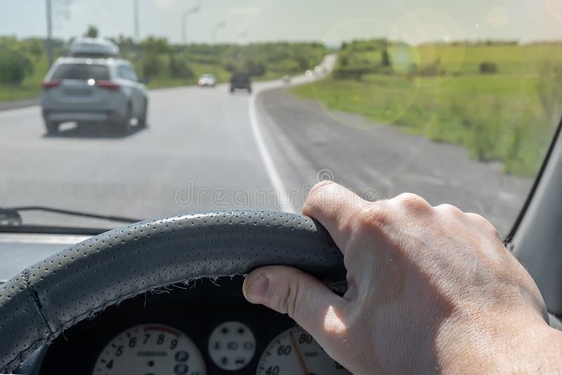Driver Hand on the Steering Wheel of a Car that is Passing on a Country