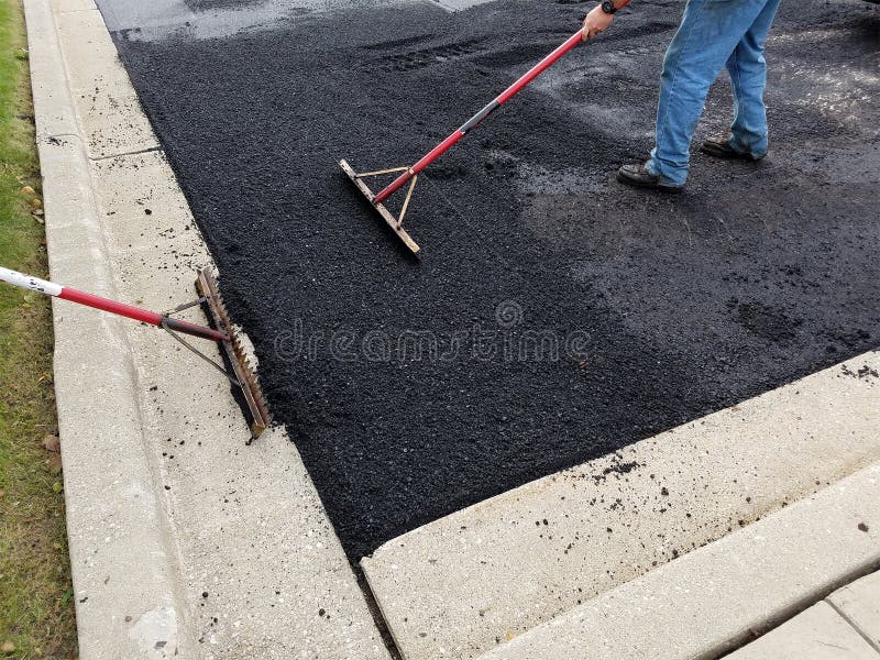 A worker is heating asphalt for a driveway parking lot. Building construction and maintenance repair is an ongoing task for contractor workers. A worker is heating asphalt for a driveway parking lot. Building construction and maintenance repair is an ongoing task for contractor workers.