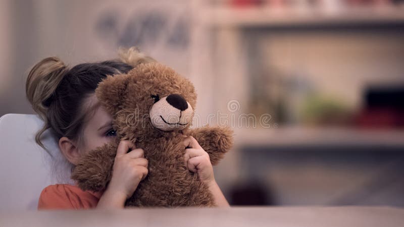 Droevig vrouwelijk jong geitje die gezicht door teddybeerstuk speelgoed, familieprobleem, eenzaamheidsmisbruik behandelen royalty-vrije stock foto Droevig vrouwelijk jong geitje die gezicht door teddybeerstuk speelgoed, familieprobleem, eenzaamheidsmisbruik behandelen royalty-vrije stock foto