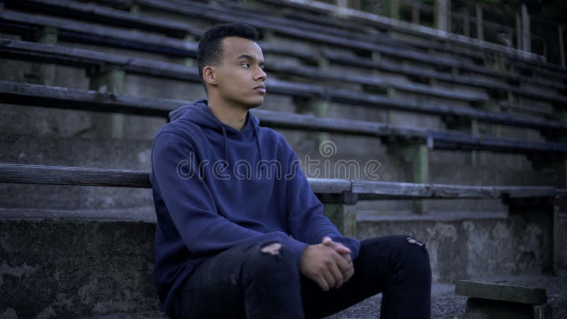Droevige Afrikaanse Amerikaanse tienerzitting op tribune, verwoesting en armoede rond royalty-vrije stock foto Droevige Afrikaanse Amerikaanse tienerzitting op tribune, verwoesting en armoede rond royalty-vrije stock foto