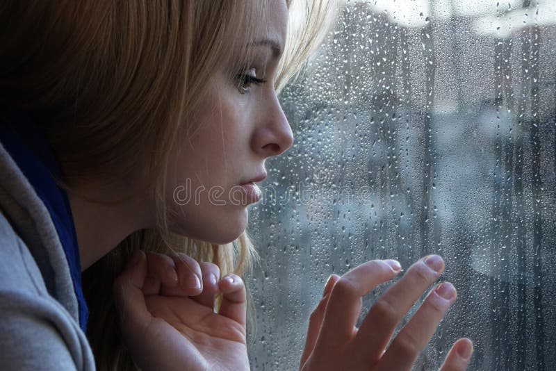 Droevige jonge vrouw die door venster op regenachtige dag kijken