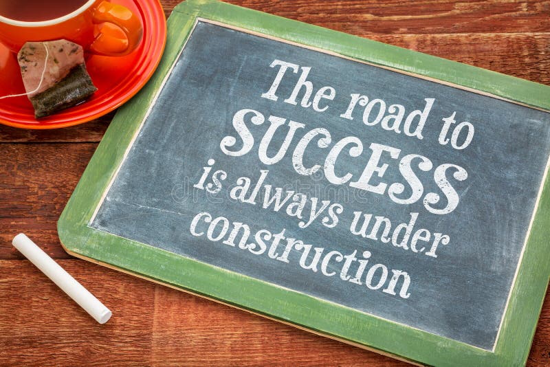 The road to success is always under construction - motivational text on a slate blackboard with chalk and cup of tea. The road to success is always under construction - motivational text on a slate blackboard with chalk and cup of tea