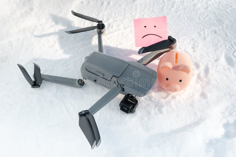Drone after crash, sticky note with sad smile and piggy bank on snow royalty free stock images