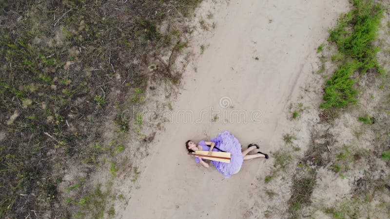 Drone filmando uma mulher harpista deitada na areia do deserto e brincando de harpa