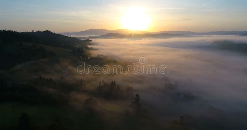 Drone flight over dreamy foggy mountain village during sunrise