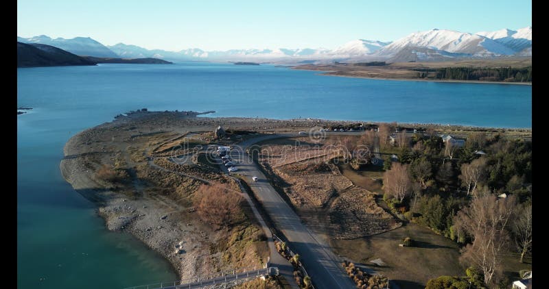 Drone flying above Lake Tekapo with a bridge over it and dam towards a snowy mountain in New Zealand stock video