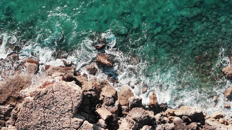 Drone flying along rocky beach. Beautiful coastline with waves. Aerial view of big sea rocks. Top view of big waves hitting seasho