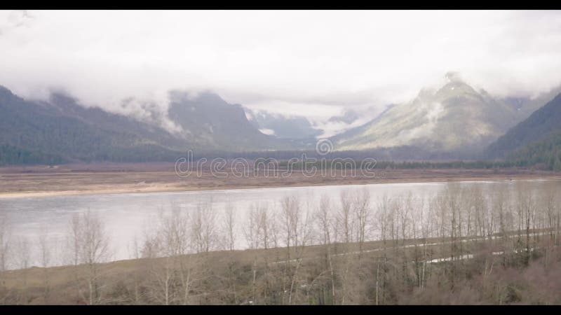 Drone flying behind leafless trees to reveal beautiful view of lake and snowy mountain stock video footage