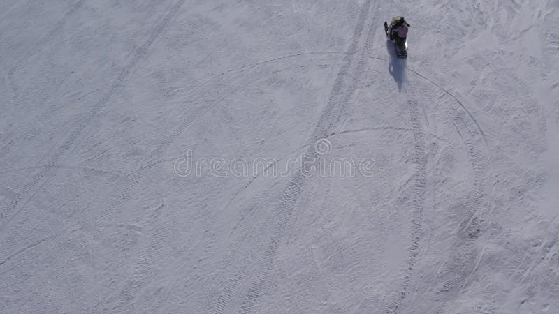 Drone footage of a snowmobile driving up to the peak of snowy mountain stock footage
