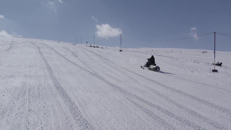 Drone footage of a snowmobile driving up to the peak of snowy mountain stock video