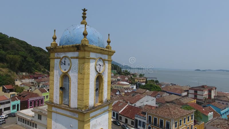 Drone shot captura una ciudad costera con una iglesia que tiene un techo azul en un día soleado. metrajes