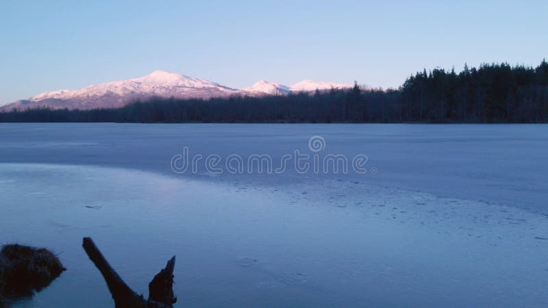 Drone view of a frozen lake at sunset with dark forest and snowy mountain in Alaska stock video footage