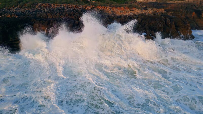 Drone view rough ocean waves crashing on coastal cliffs. Sea surf lapping beach