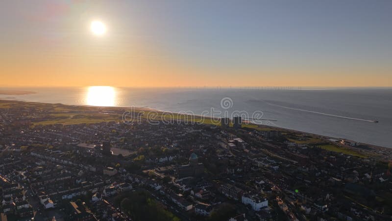 Drones sobrevolando una ciudad costera hacia el océano con agua que reflejaba la luz de la puesta del sol metrajes