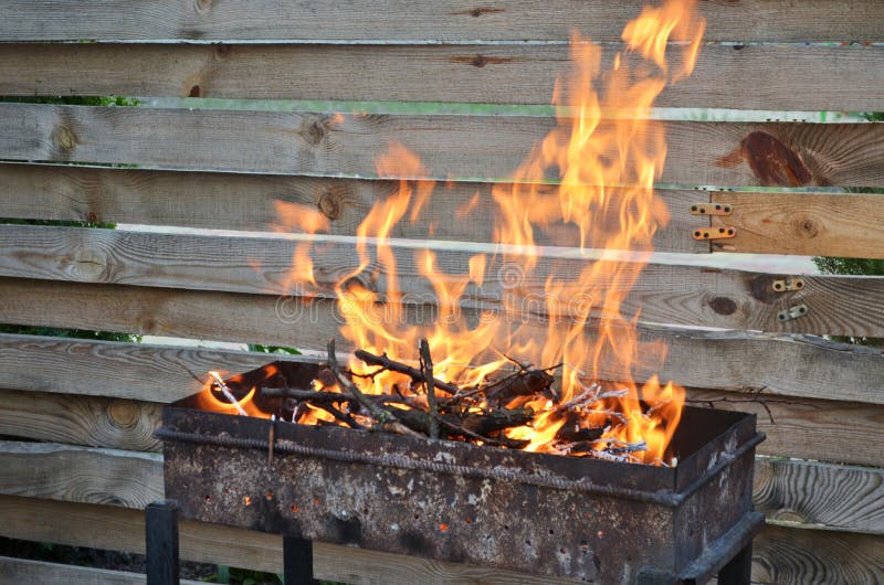 Droog hout voor het roosteren van brandwond met een grote vlam op de grill, op een achtergrond van een houten omheining royalty-vrije stock afbeeldingen Droog hout voor het roosteren van brandwond met een grote vlam op de grill, op een achtergrond van een houten omheining royalty-vrije stock afbeeldingen