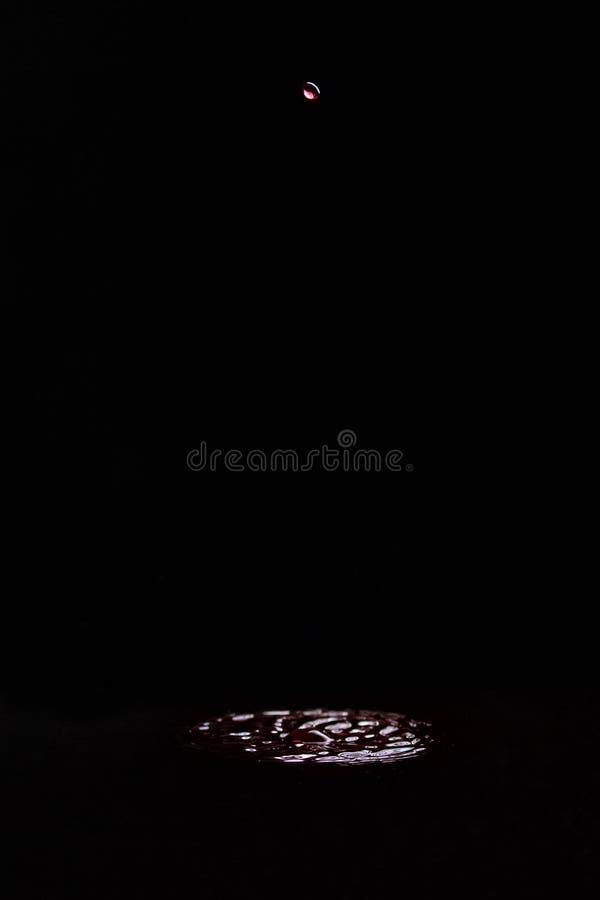 A drop of red wine falling into wine on a black background. Splash, circles on the surface from the fallen drop.