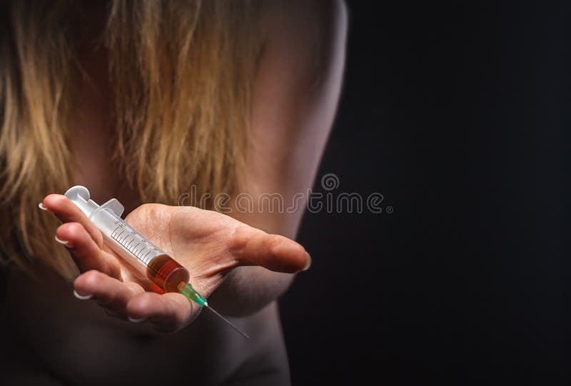 A young woman with a drug holding a syringe on dark background