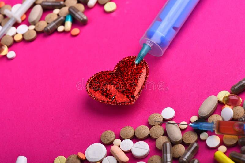 Drugs near heart with syringe inside. Set of colorful pills scattered on pink background. Frame made of pills and capsules put on sides. Heart disease and medicine concept.