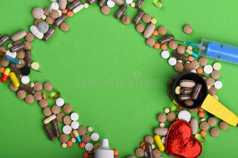 Drugs near syringe, heart and measuring spoon. Heart disease and medicine concept. Set of colorful pills scattered on green background, copy space. Frame made of pills and capsules put in rectangle