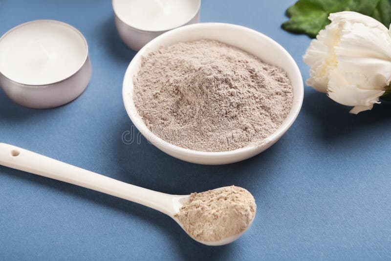 Dry cosmetic mud mask powder in bowl on blue background