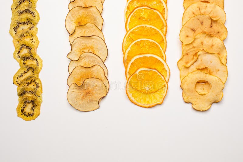 The dry pieces of different fruits in a row to fresh fruits. Top view of row of different dried fruits lying on a white background.