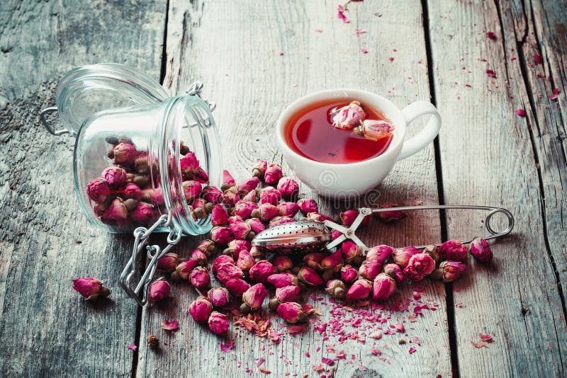 Dry rose buds, tea cup, strainer and glass jar with rosebuds.