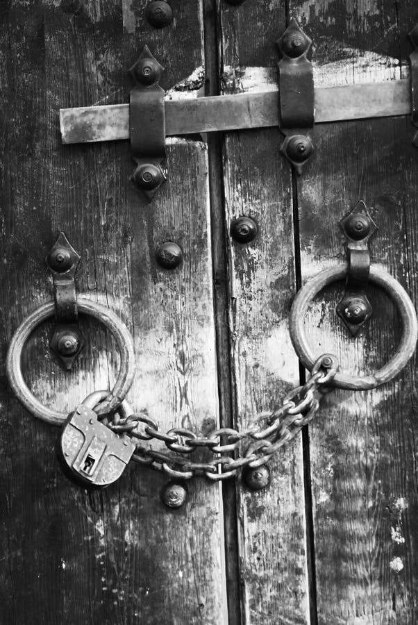 Heavy wooden doors with chains and padlocks are all about security. Black and white photo of castle portal. Heavy wooden doors with chains and padlocks are all about security. Black and white photo of castle portal.