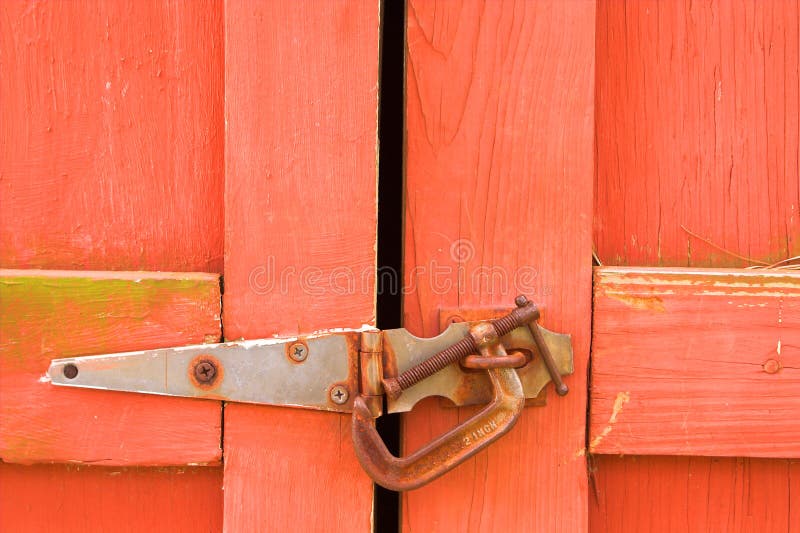 An old red barn door with a c-clamp for a lock. An old red barn door with a c-clamp for a lock.