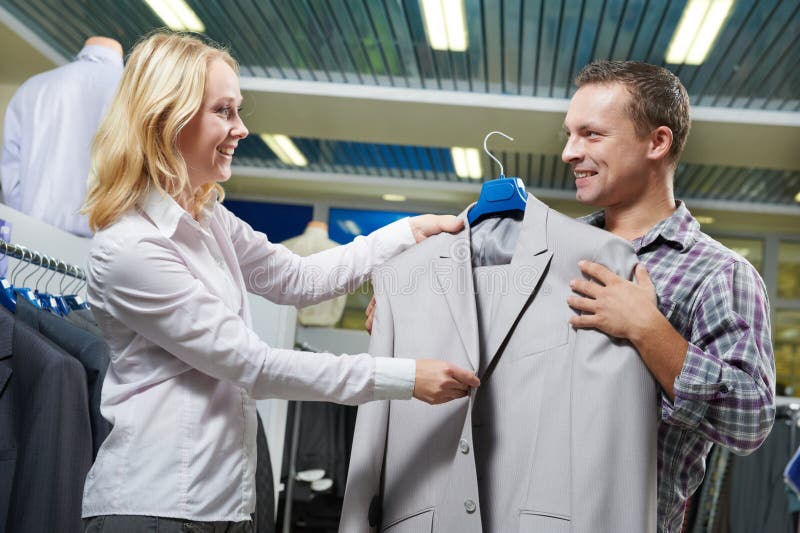 Dräktshopping säljaren visar den formella dräkten till mannen i lager royaltyfri bild Dräktshopping säljaren visar den formella dräkten till mannen i lager royaltyfri bild