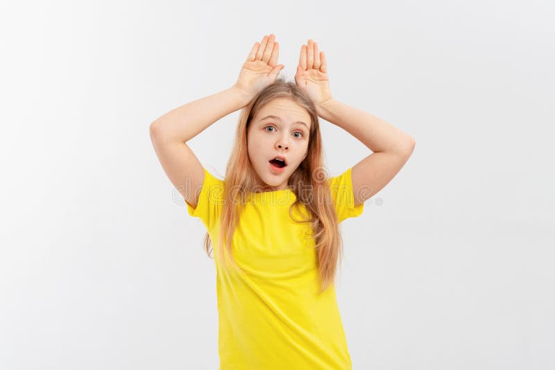 Drôle adolescente debout sur fond blanc faire des oreilles lapin gestes avec les mains palmiers avoir l'air heureux et heureux. la photo stock