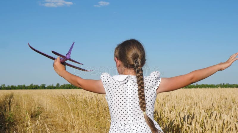 Drömmar om att flyga och bli pilot. en glad flicka flyger med ett leksaksflygplan på ett vetefält under blå himmel