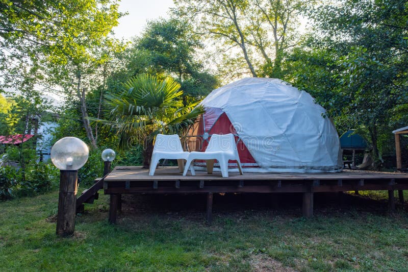 Geodesic dome tent on a raised wooden deck in a lush green glamping site stock photo