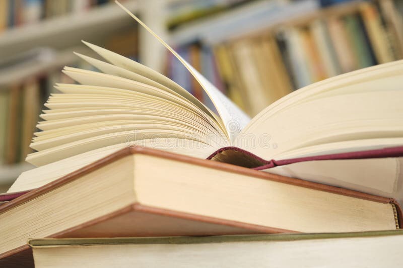 Open book or textbook on a pile of closed books in front of a bookcase stock image
