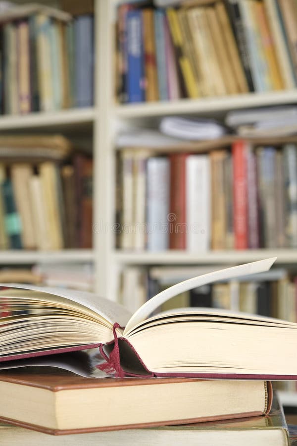 Open book or textbook on a pile of closed books in front of a bookcase royalty free stock photo