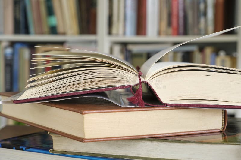 Open book or textbook on a pile of closed books in front of a bookcase royalty free stock photos