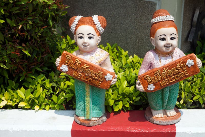 Duas estatuetas cerâmicas das meninas tailandesas que guardam bem-vindas assinam dentro inglês e tailandês imagens de stock Duas estatuetas cerâmicas das meninas tailandesas que guardam bem-vindas assinam dentro inglês e tailandês imagens de stock