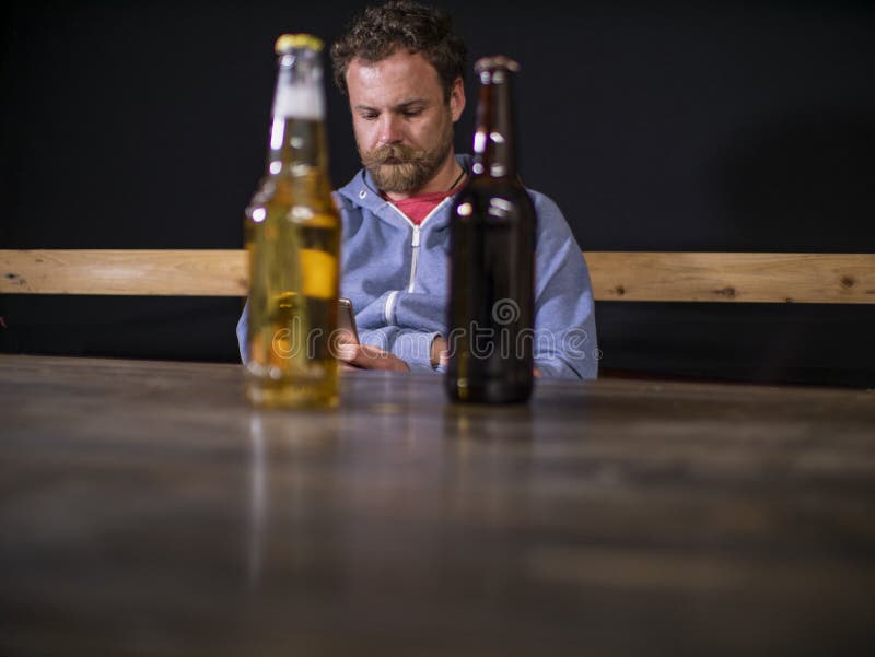 Duas garrafas da cerveja estão estando na tabela na perspectiva de um homem de assento que olhe no telefone fotografia de stock Duas garrafas da cerveja estão estando na tabela na perspectiva de um homem de assento que olhe no telefone fotografia de stock