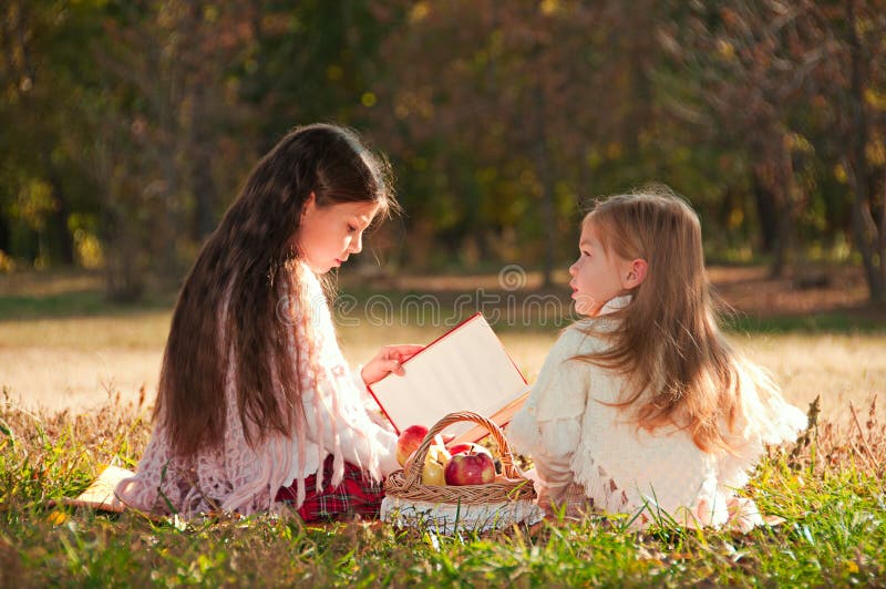 Duas irmãs das meninas leram o livro na grama foto de stock royalty free Duas irmãs das meninas leram o livro na grama foto de stock royalty free