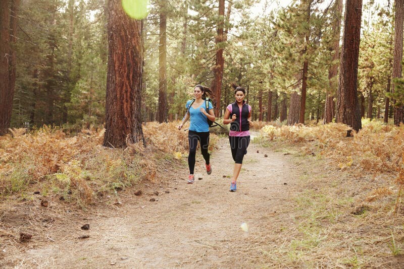 Duas jovens mulheres que correm em uma floresta foto de stock Duas jovens mulheres que correm em uma floresta foto de stock